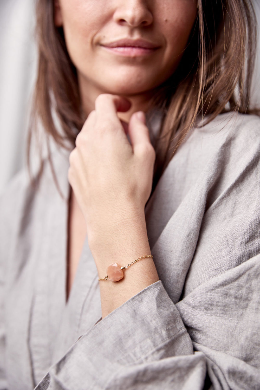 PAUKAA Armband gold mit Mondstein rosé und goldenem NAIONA Plättchen. Pose, Arm, Handgelenk, Bluse.
